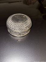 Closed round metal trinket box showing ornate exterior design and tarnish