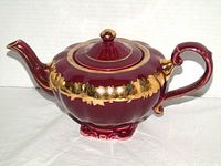 Side view of burgundy ceramic teapot with gold band and lid