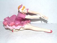 side view of porcelain ballerina in pink tutu stretching forward