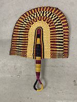 Full view of woven straw wall fan showing colour pattern and handle loop