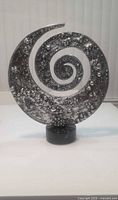 Front view of metal spiral sculpture on stone pedestal