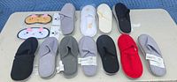 Lot overview showing 11 pairs of slippers in various colors and 2 packaged cat sleep masks