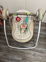 Full view of portable baby swing with toy bar and plush toys attached