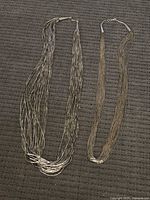 Both liquid silver necklaces laid flat showing overall design and clasps