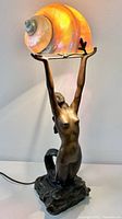 Front view of bronze mermaid lamp with shell shade illuminated