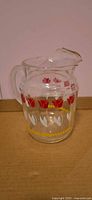Front view of clear glass pitcher with tulip decals and yellow band