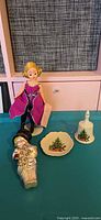 Group shot of doll, porcelain plate, porcelain bell, glass snowman ornament