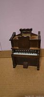 Front view of miniature wooden pump organ music box showing keyboard and pedal