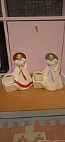 Front view of both lady figurine planters showing red and blue trim and planter compartments