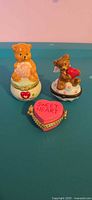 Front view of three porcelain trinket boxes showing teddy bear figures and pink heart box