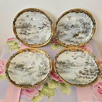 Front view of all four Japanese porcelain plates showing painted scenes and gold gilt rims