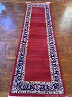 Full view of runner rug showing red field, bordered design, hardwood floor backdrop