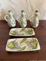 Front view of three matching cruet pitchers and two butter dishes showing Wild Grapes pattern