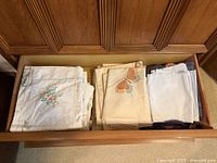 Drawer view showing stacks of embroidered white linens, butterfly print linens and plaid throw