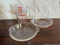 Two Pyrex measuring cups stacked, two Pyrex pie dishes side by side on wood surface