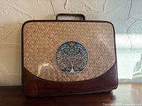 Front view of woven wicker briefcase with leather trim and tree motif