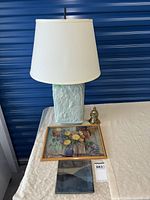 group shot of all four items: lamp, framed picture, brass bell, ceramic plate