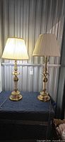 Two matching brass-tone and cream table lamps lit, showing overall design and shades