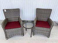 Pair of resin wicker armchairs with red cushions and glass-top bistro table