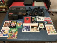 Overall lot showing console, controllers, cartridges, manuals and catalogs on table
