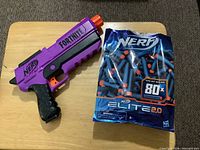 Front view of Nerf Fortnite purple dart blaster beside sealed bag of Nerf Elite 2.0 darts