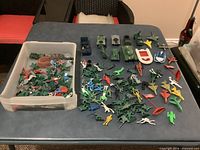 Overall view of tote and spread-out plastic army men and vehicles on table