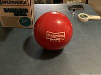 Full view of red Brunswick bowling ball beside original box