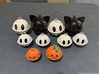 Full group of 10 metal Halloween jingle bells—2 black cats, 6 white ghosts, 2 orange pumpkins arranged on table