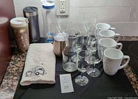 All items arranged on countertop: stemware, mugs, carafe, tumblers, towel