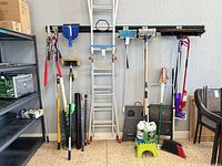 Full lot view against wall with ladder showing step stools, brooms, loppers, poles and cleaners