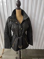 Front view of black quilted jacket on mannequin with belt and gold-tone hardware visible