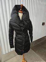 Front view of black long puffer coat on mannequin showing quilting, collar, length