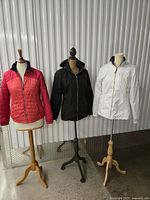 Front view of three jackets on stands: red, black, white