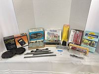 Overall view of boxed and loose HO-scale model railroad items including pier set, structure kit, freight cars, power pack, track and scenery parts