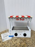 Front angled view of hot dog roller showing canopy, control panel, rollers, manual, power cord