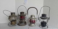 Front view of four vintage railroad lanterns showing globes, wire guards and handles