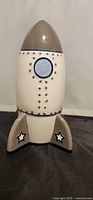 Front view of ceramic rocket coin bank showing nose cone, window and star-decorated fins