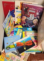 Stack of assorted children’s books and board books including Disney Frozen, Charlie Brown, Smurfs, Strawberry Shortcake, Eric Carle, touch-and-feel and others