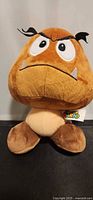 Front view of Goomba plush showing full figure and tag