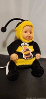 Full view of seated bumblebee baby doll with costume and hang tag