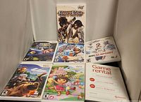 Front view of seven Wii game cases displayed upright: Prince of Persia, Super Mario Galaxy, All Star Karate, NHL Slapshot, Up, Dora, generic Game Rental case