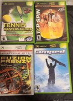 Front view of four Xbox game cases: Tennis Masters Series, Top Spin, Fuzion Frenzy, Amped