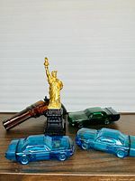 Group of five Avon novelty bottles: two blue Mustangs, green Mustang, pistol, Statue of Liberty