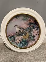 Front of porcelain plate in round white frame showing bird and blossom artwork