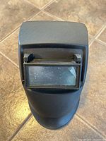 Front view of black welding helmet showing rectangular lens with crack