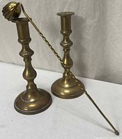Two brass candlesticks and brass snuffer laid out on white surface