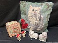 Group shot of all cat-themed items: pillow, tin, shakers, figurines