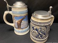 Both steins side by side showing artwork, lids, handles