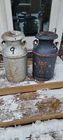 Both milk cans side by side on snowy wooden surface showing overall condition and size