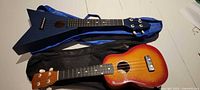 Both ukuleles in their gig bags, sunburst Beaver Creek and blue Flying V Bravo
